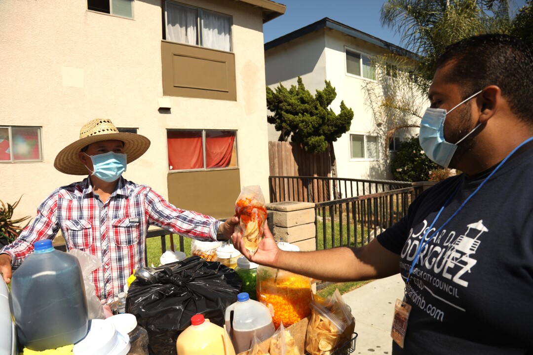 Longtime community activist Oscar Rodriguez, right, buys a bag of chips from street vendor Fernando Aguilar in Oak View.