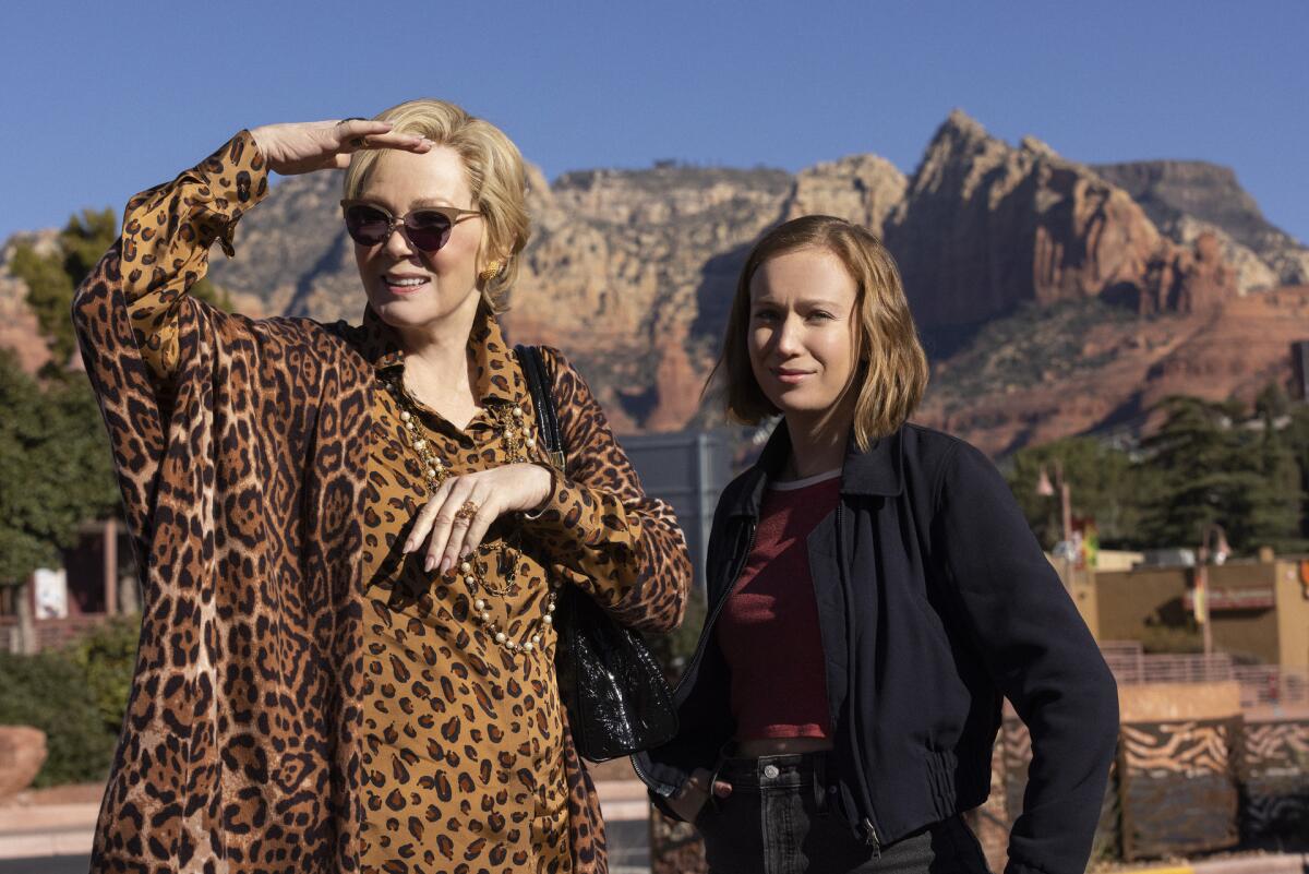 Two women, one in leopard print clothes, stand outside with hills in the background.