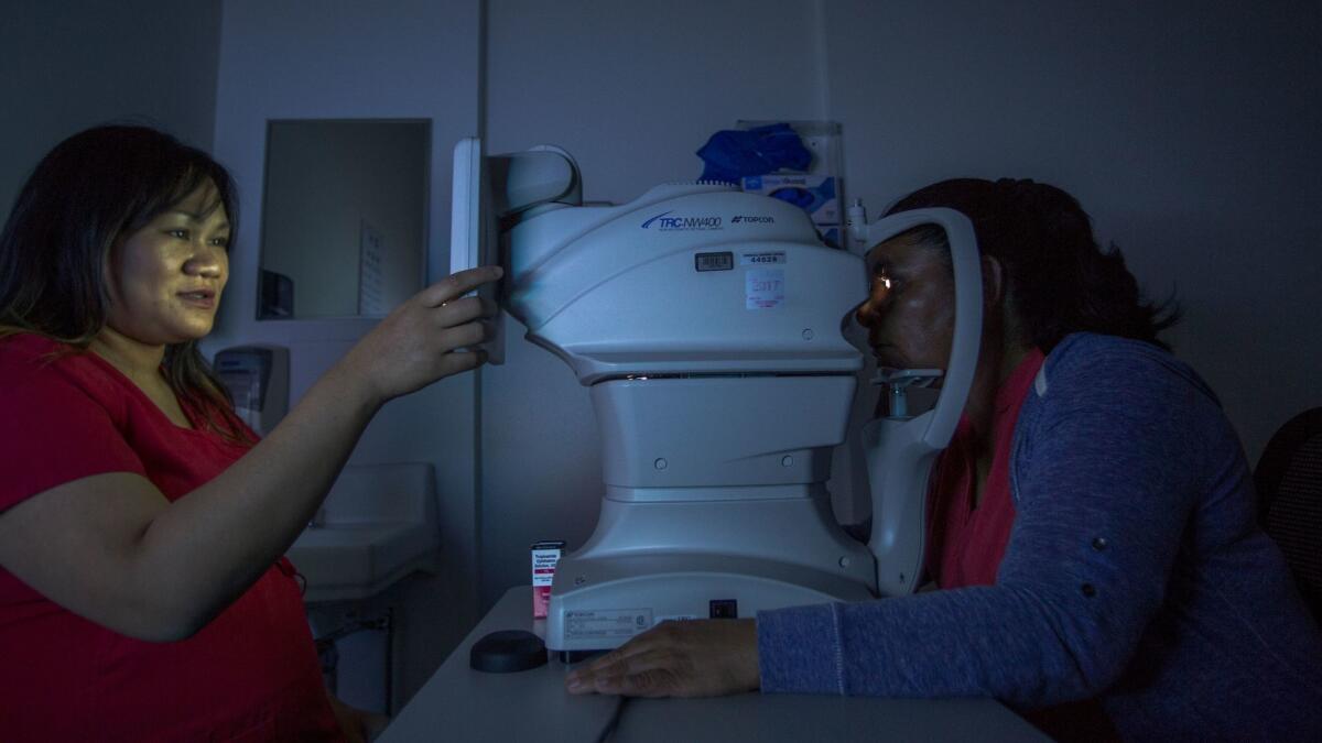 Un destello de luz ilumina el ojo de Juana Lorez (derecha) mientras Bea Tomayo fotografía su retina en el Los Angeles County-USC Medical Center (David McNew / para The Times).