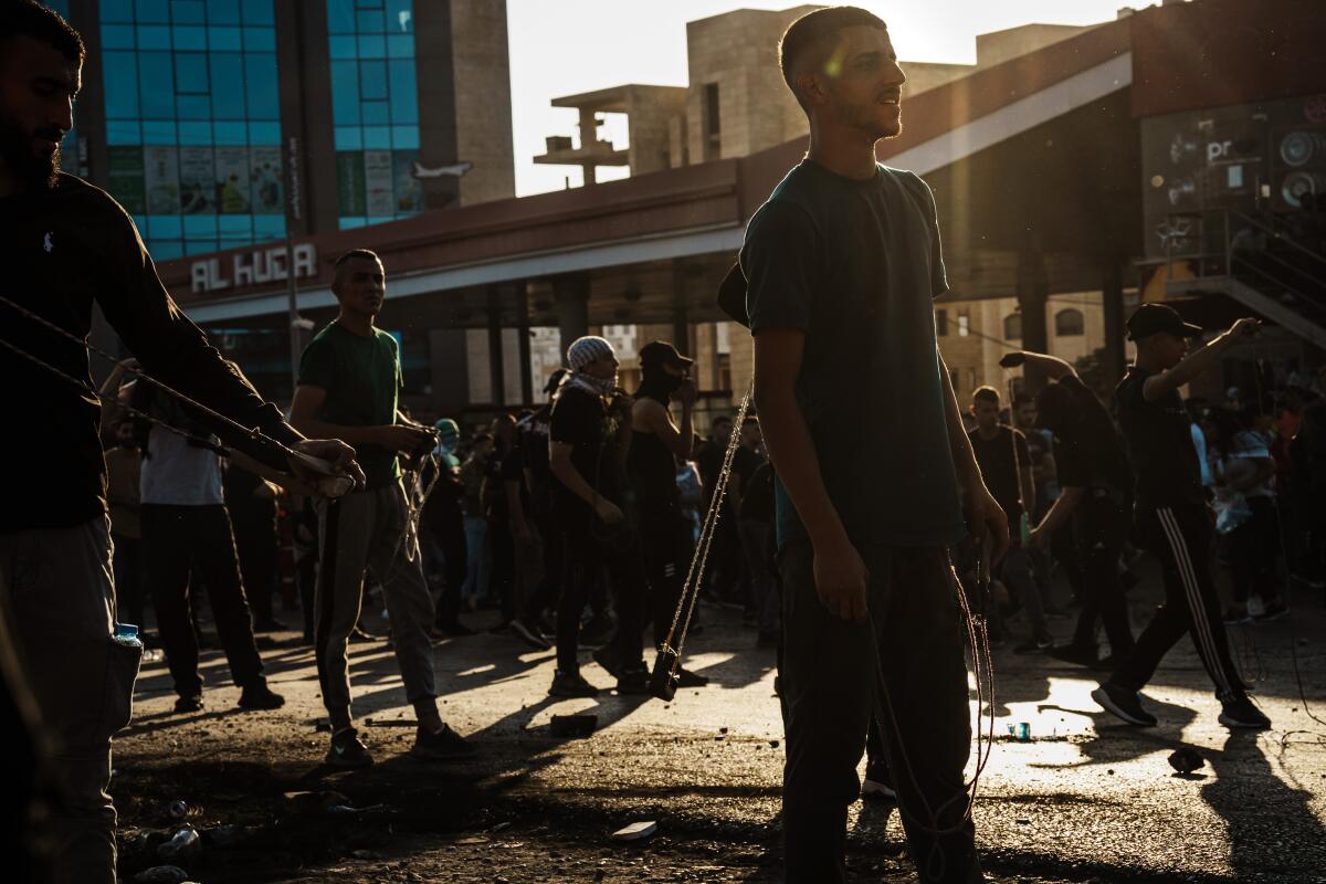 Palestinian men bearing slings stand in protest in Ramallah against the setting sun.