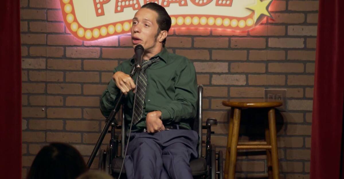 A man in a wheelchair holds a mic onstage.