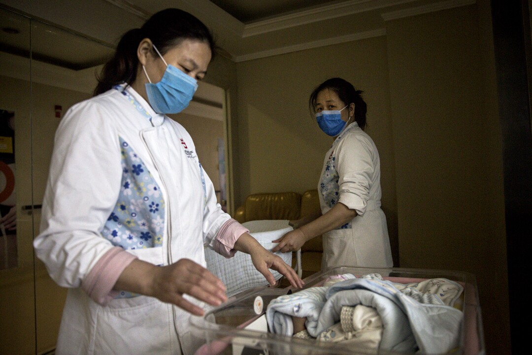 A maternity nurse wears a mask as she cares for a newborn.