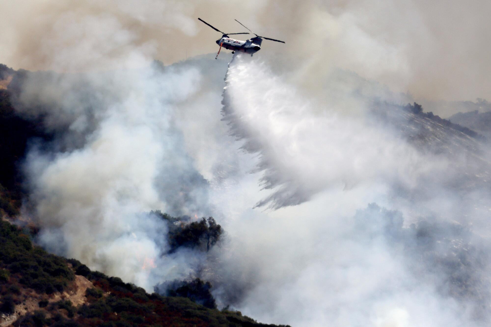 A helicopter drops water on a fire.