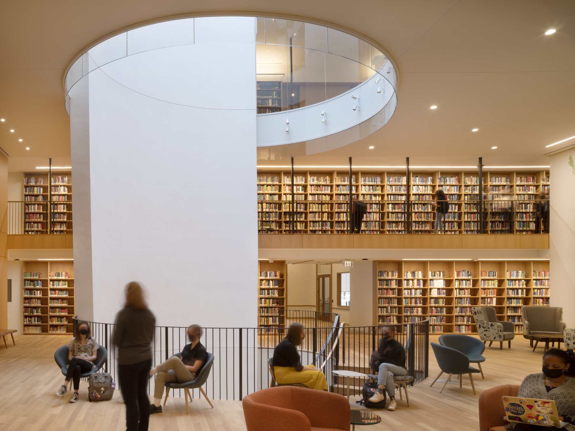 Students sit and stand in an airy two-story area lined with bookshelves that's pierced by an oculus.