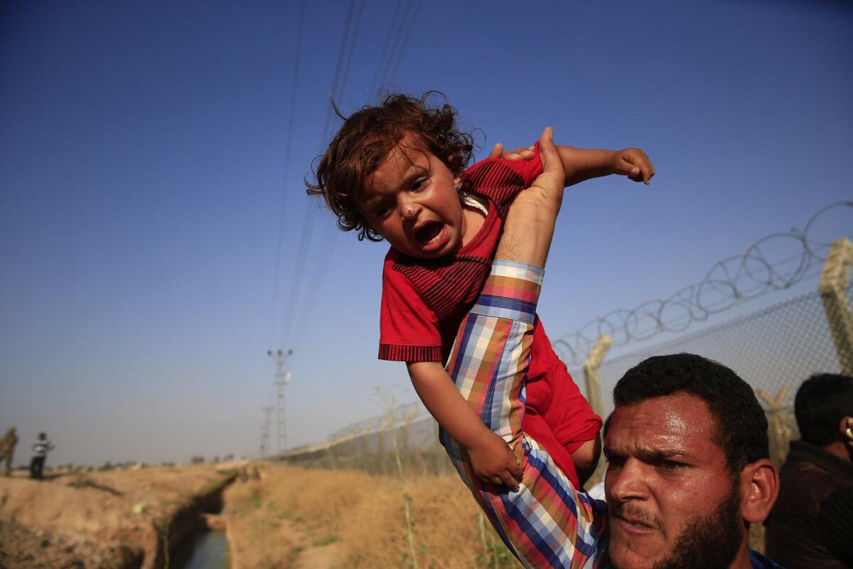 A Syrian refugee carries a baby aloft after crossing over the broken border fence into Turkey from Syria in Akcakale.
