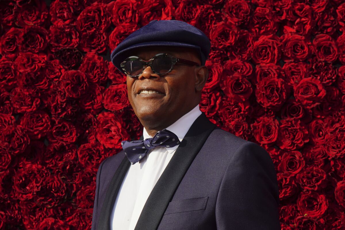 Samuel L. Jackson in a hat, sunglasses and suit poses against a backdrop of roses