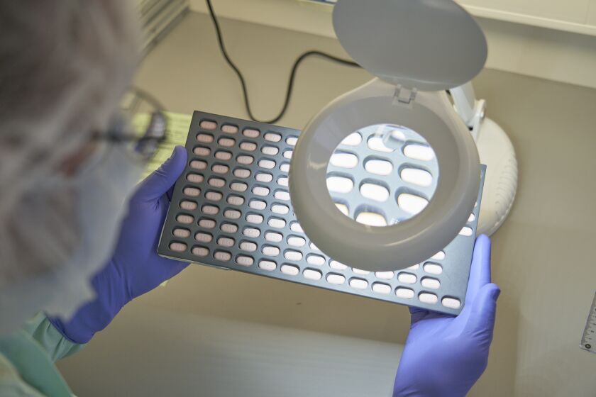 In this photo provided by Pfizer, a lab technician visually inspects Paxlovid tablet samples in Freiburg, Germany in December 2021. Studies showed that the first pill to treat the virus led to a nearly 90% reduction in hospitalizations and deaths among patients most likely to get severe disease. (Pfizer via AP)