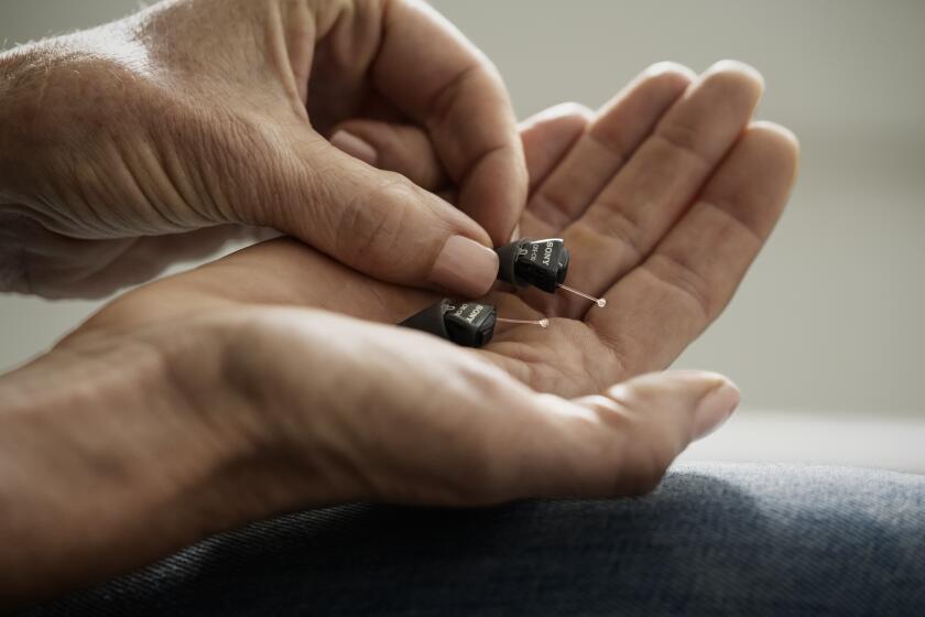 A person's hands hold the CRE-C10, a pair of self-fitting aids from Sony Electronics.