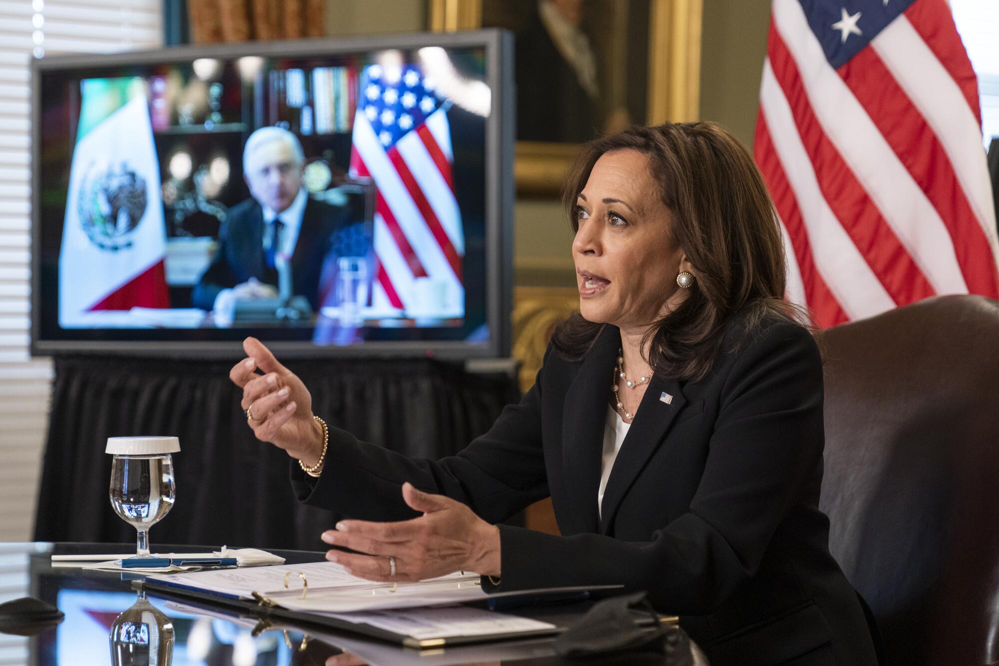 Kamala Harris gestures while speaking at a desk; behind her, Mexican President Andrés Manuel López Obrador on a monitor