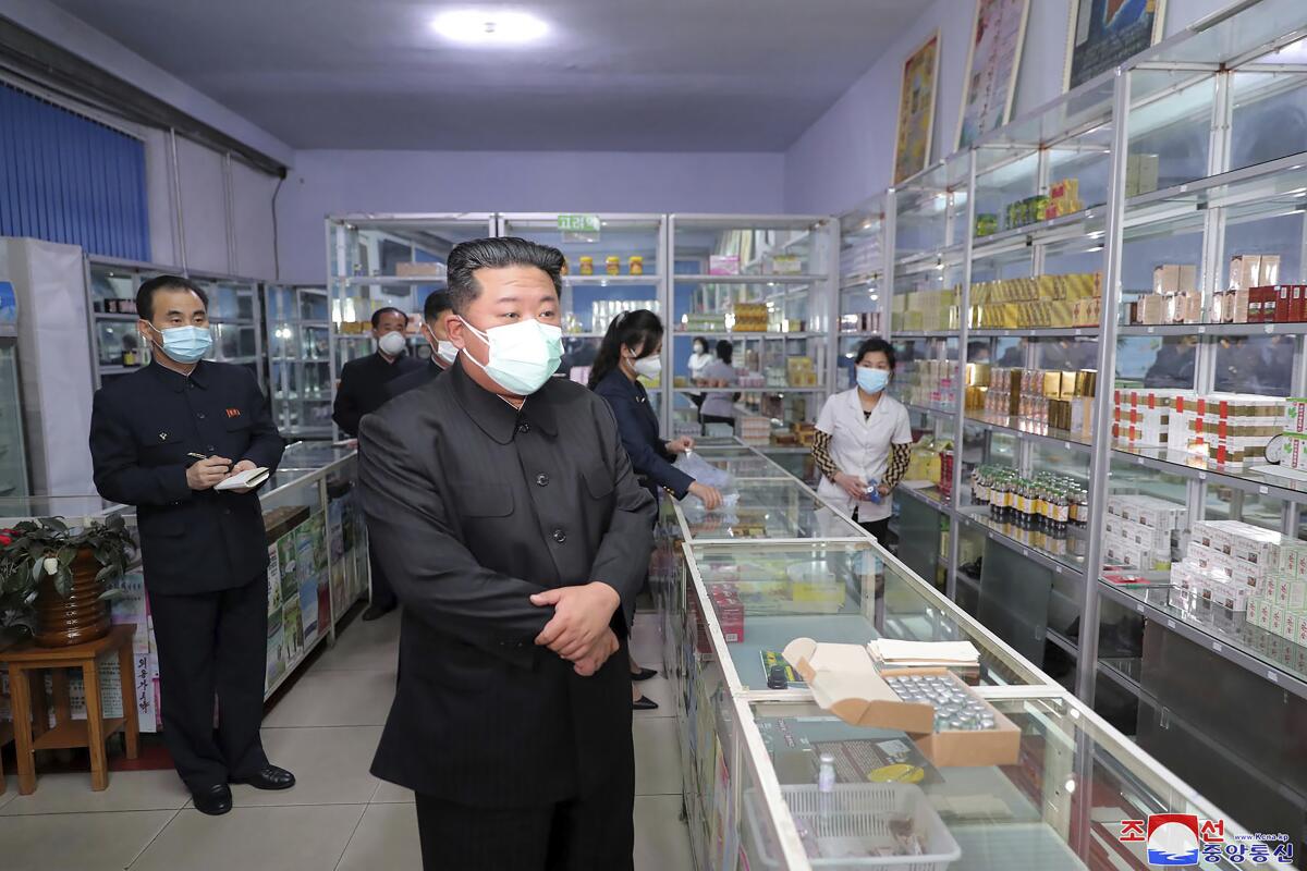Kim Jong Un wears a mask while standing at a pharmacy counter.