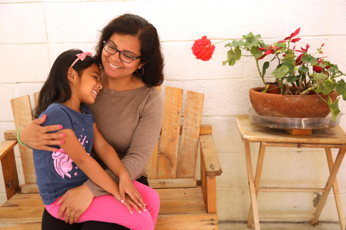 At home, DACA recipient Miriam Delgado holds her daughter Aleha Esquivel, 7, in her lap. Both are smiling.