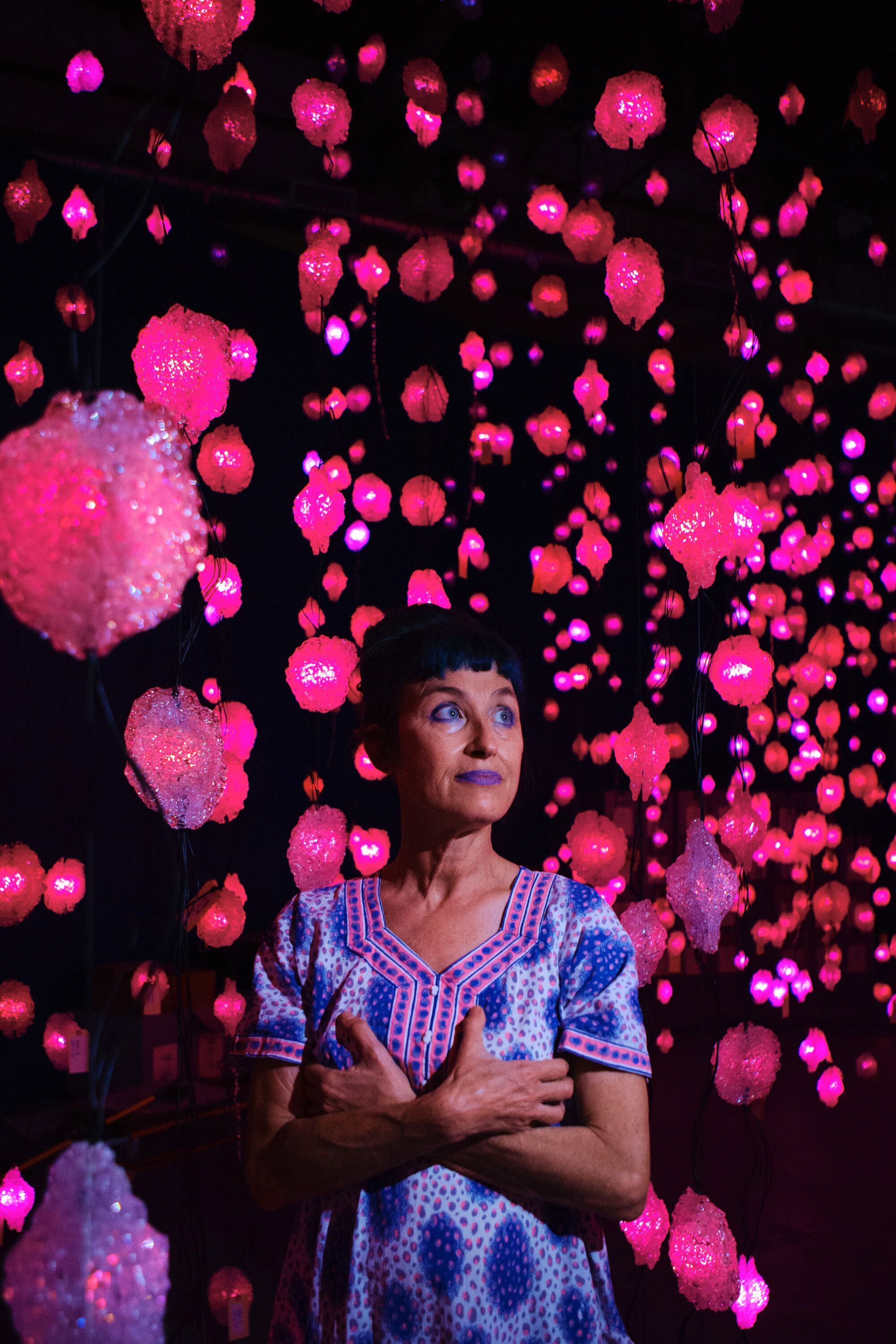 Pipilotti Rist in a blue paisley tunic stands amid dozens of pink lights