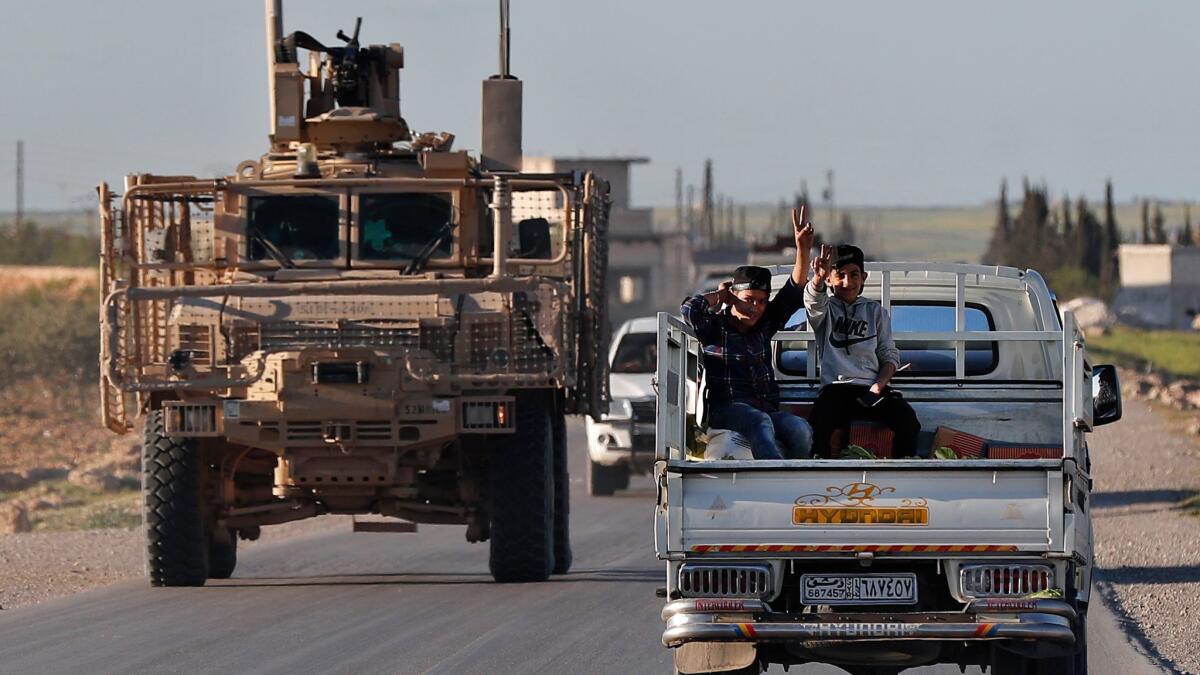 In this March 31 photo, Syrian boys travel next to a U.S. vehicle on a road leading to the tense front line with Turkish-backed fighters, in Manbij, Syria. President Trump has ordered the Pentagon to plan to withdraw U.S. troops from Syria, but held off on setting a date.