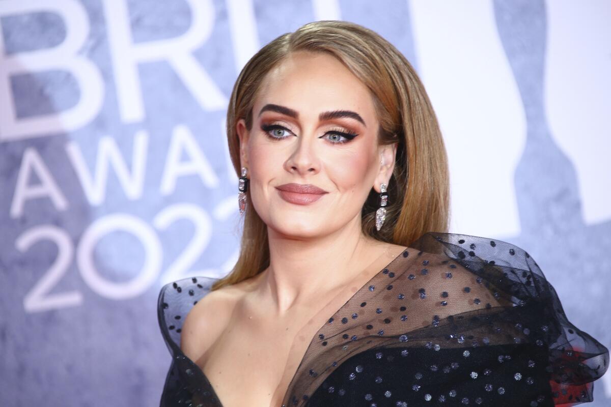 Adele wears a black dress as she poses for photos at a red carpet event.