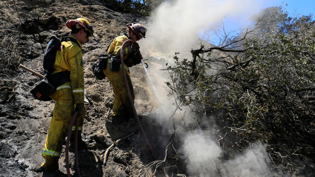 Cal Fire-San Diego firefighter Andrew Russell, left, and Capt. Angel Hendrie mop up remnants of the Sage fire in the Santa Clarita Valley.