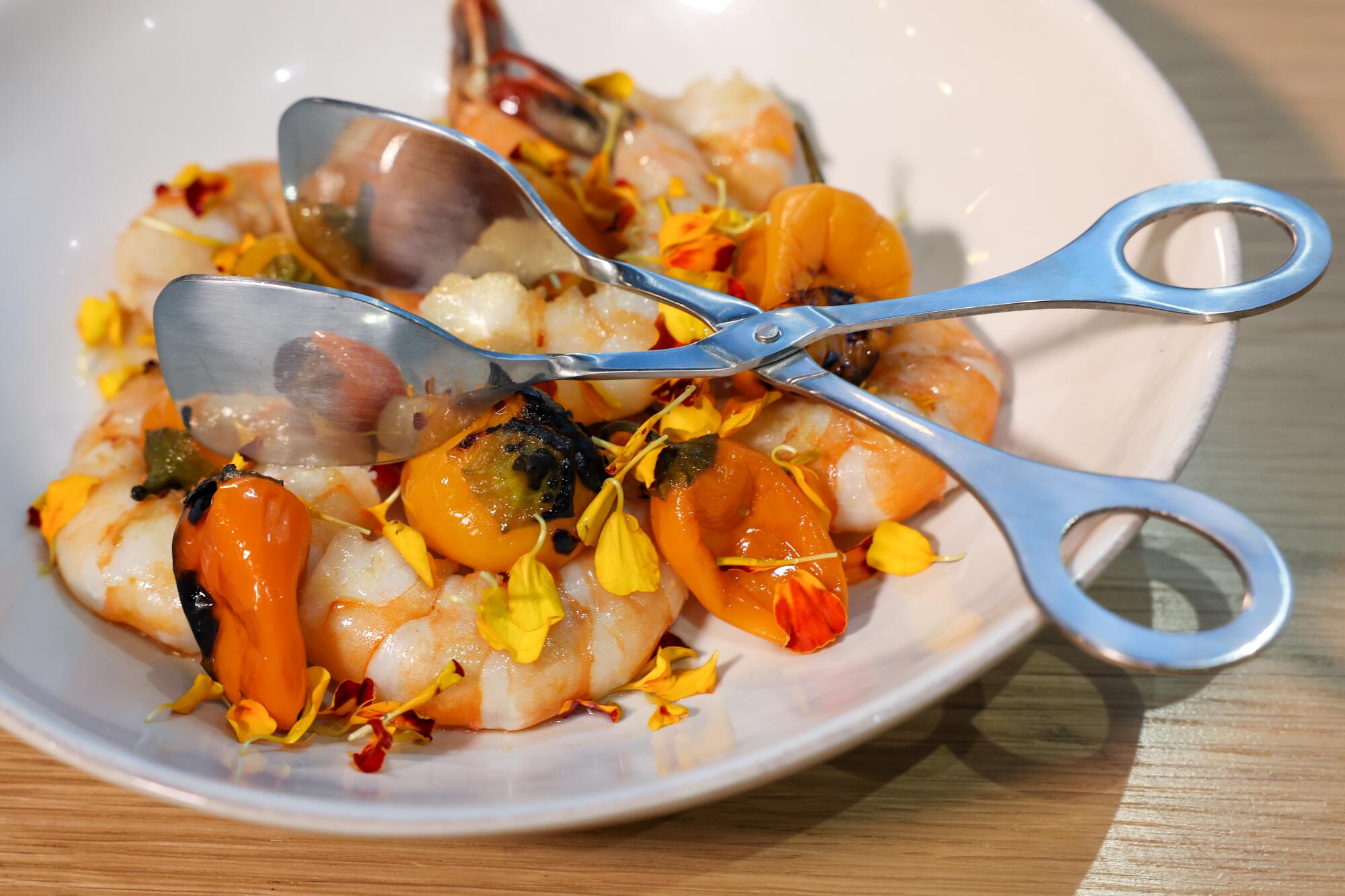 Shrimps on a plate with marigold petals and silver tongs