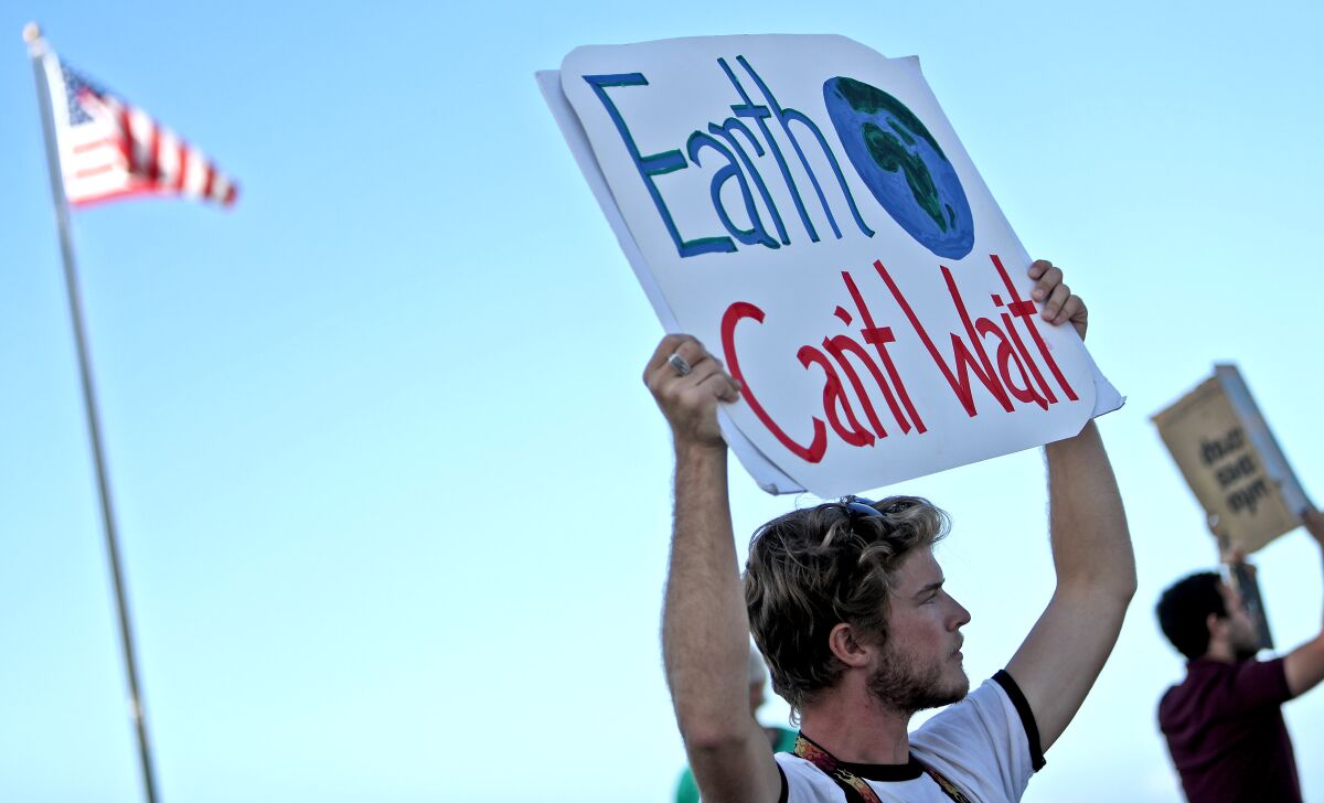 A protester at a climate strike holds up a sign, "Earth Can't Wait"