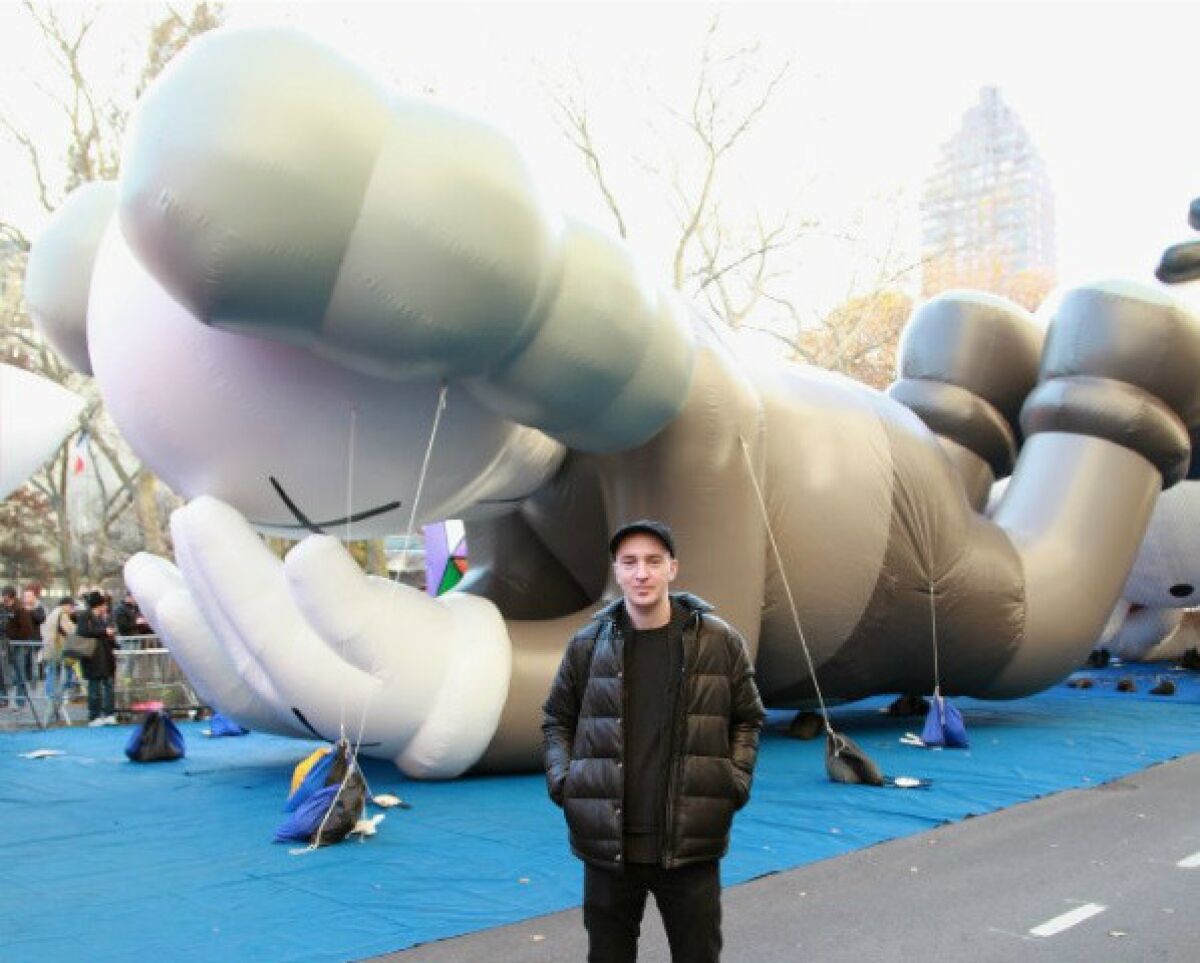 The street artist known as KAWS poses in front of his balloon "Companion" at the 86th Annual Macy's Thanksgiving Day Parade.