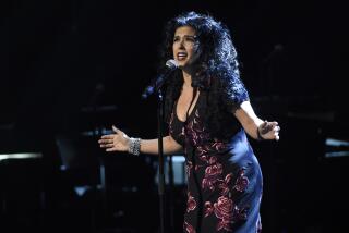 Rebekah Del Rio leaning into a microphone on a dimly lit stage with her arms outspread