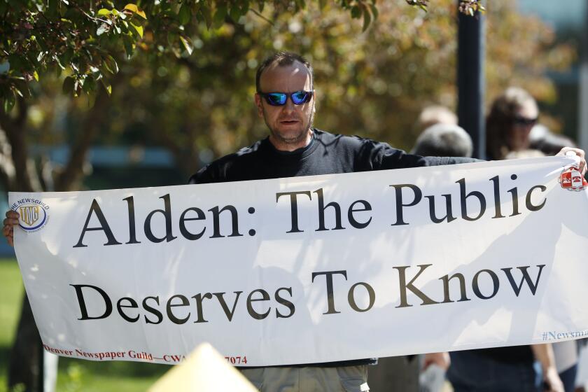 A man holding a large white banner that says, "Alden: The Public Deserves to Know."