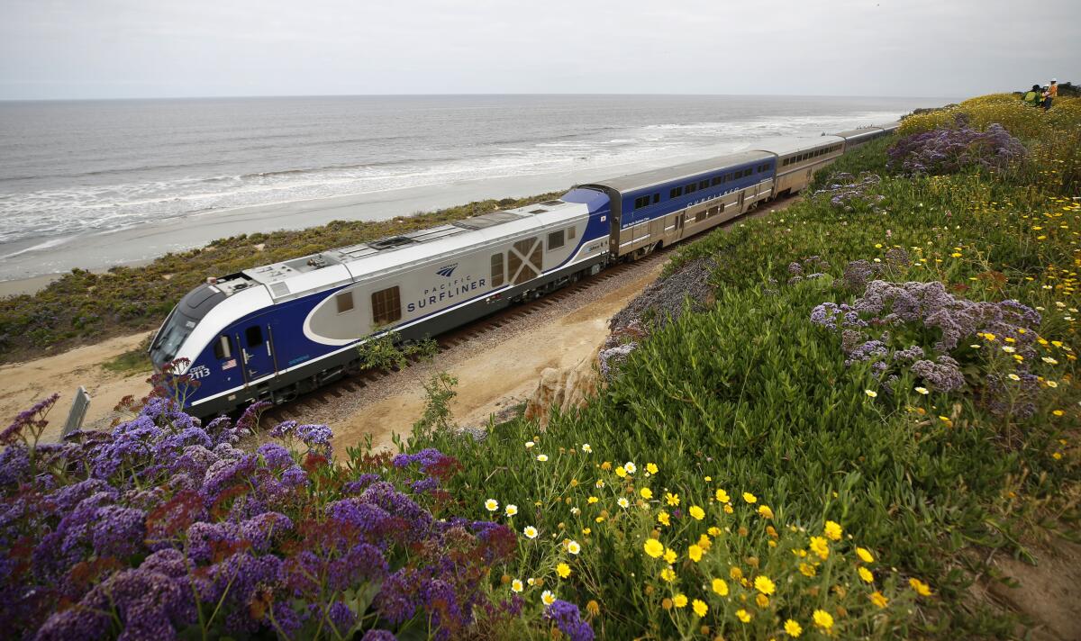 An Amtrak Pacific Surfliner train rides along the coast with the surf and sand in the background.