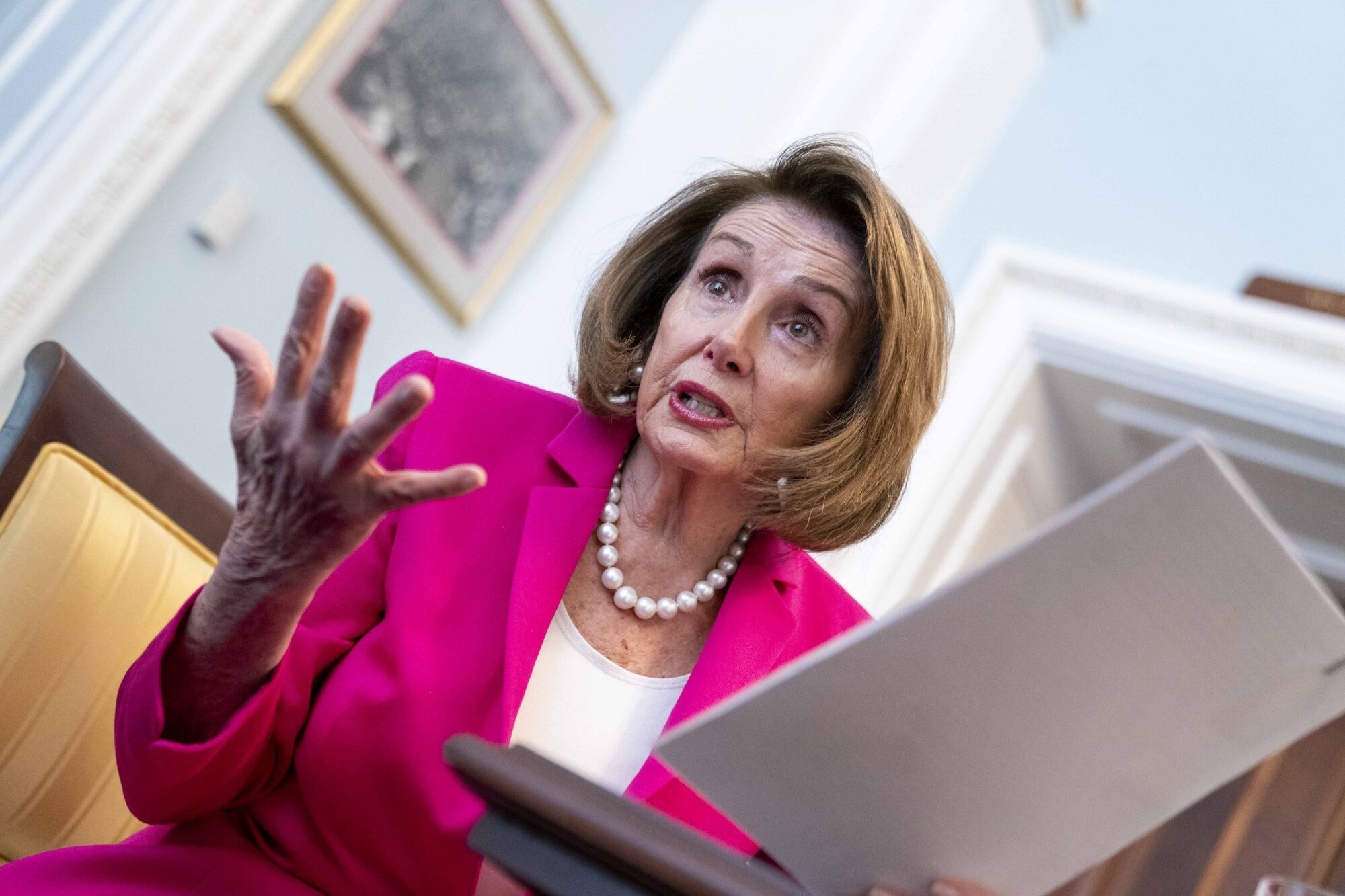 Nancy Pelosi reviews notes while speaking to another person off-camera
