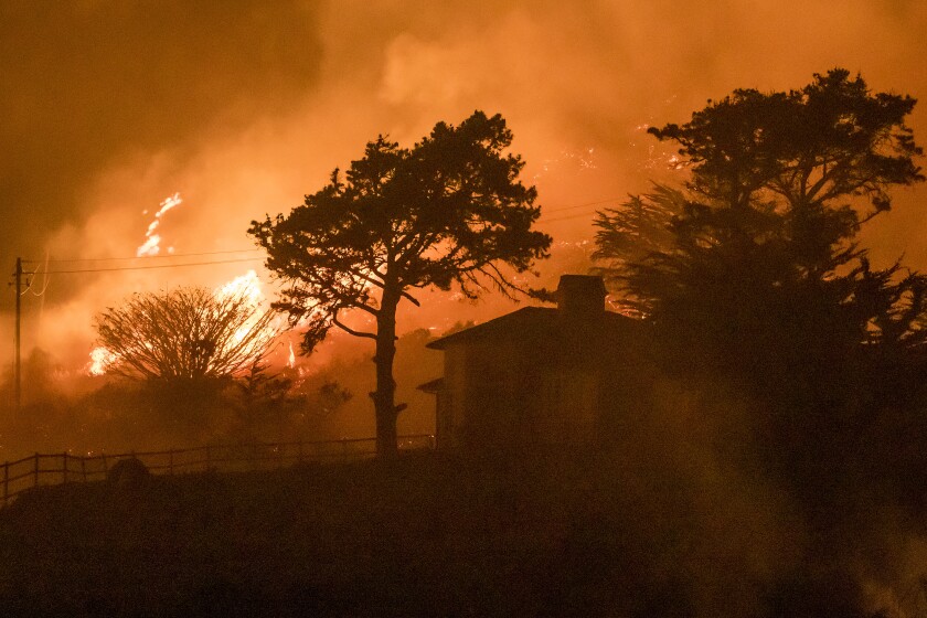 Flames burn in brush behind a house.