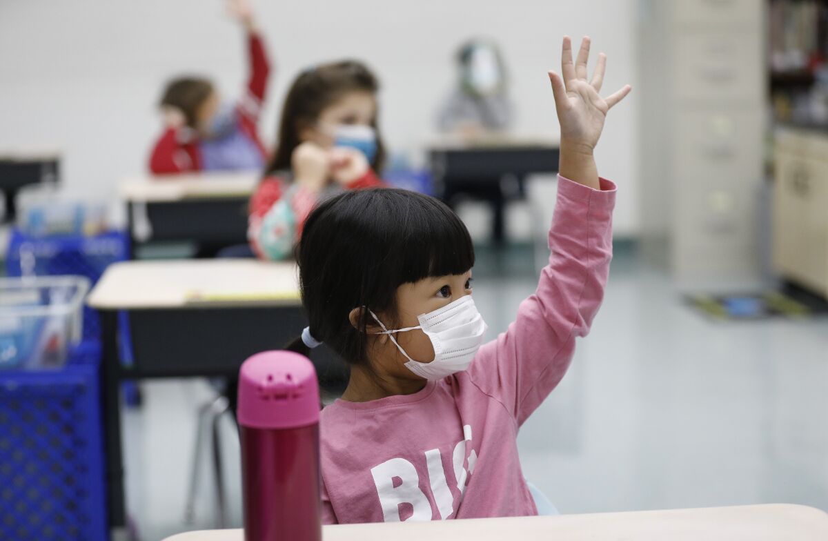 Masked elementary students raising their hands in class