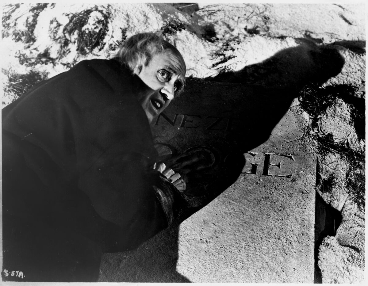 Ebenezer Scrooge (Alastair Sim) leans on his own grave marker in “A Christmas Carol” (1951)
