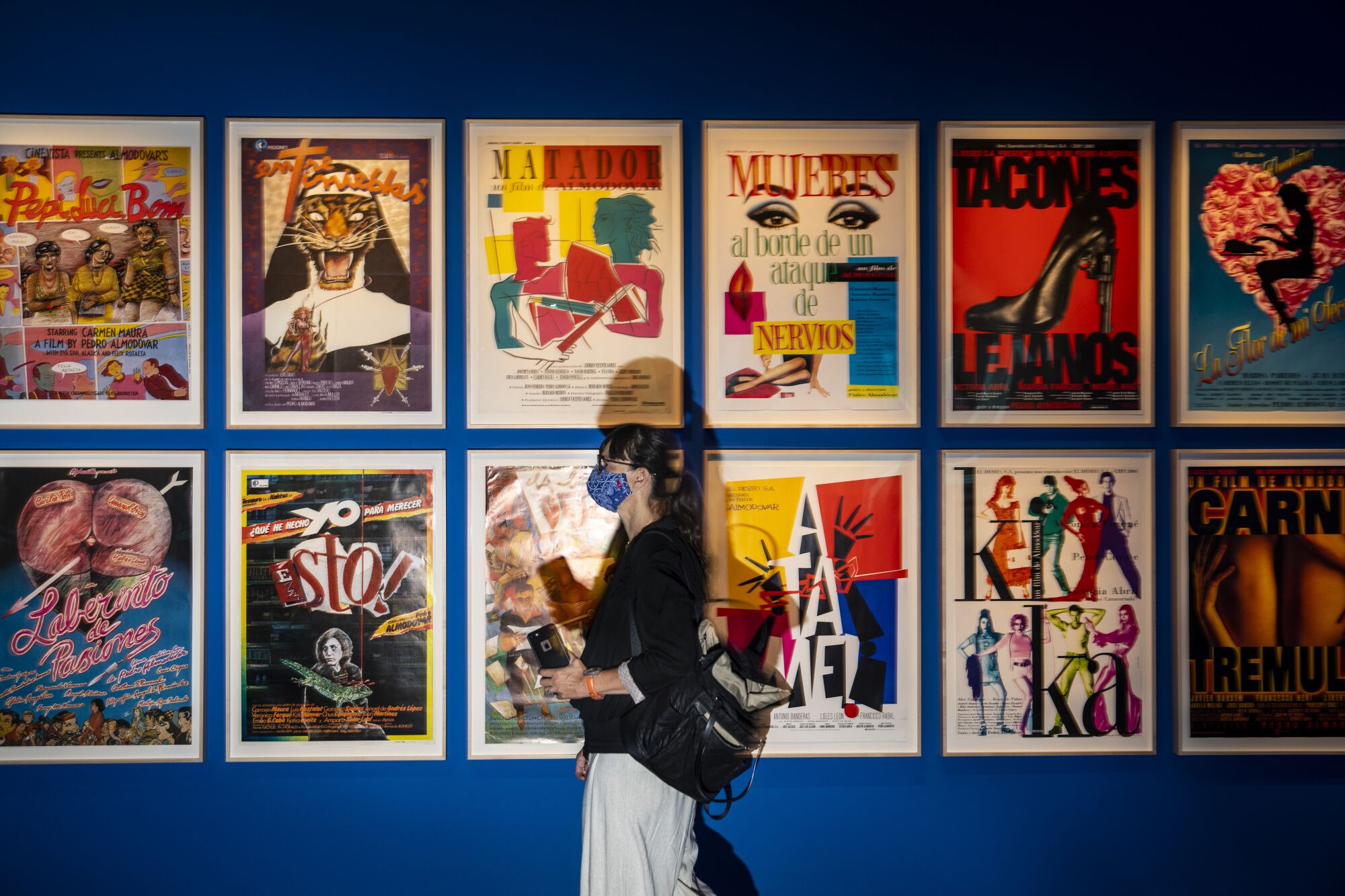 A person wearing a mask walks past a wall covered in posters