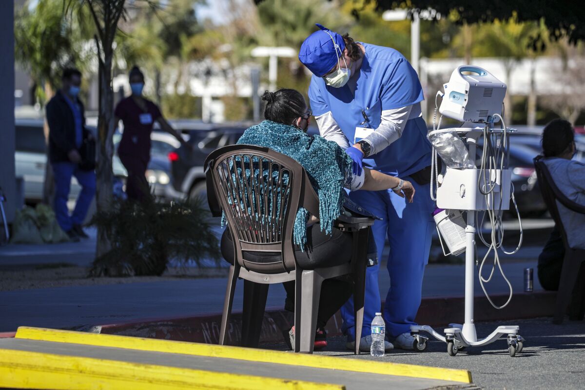 A healthcare worker examines a patient in a parking lot 