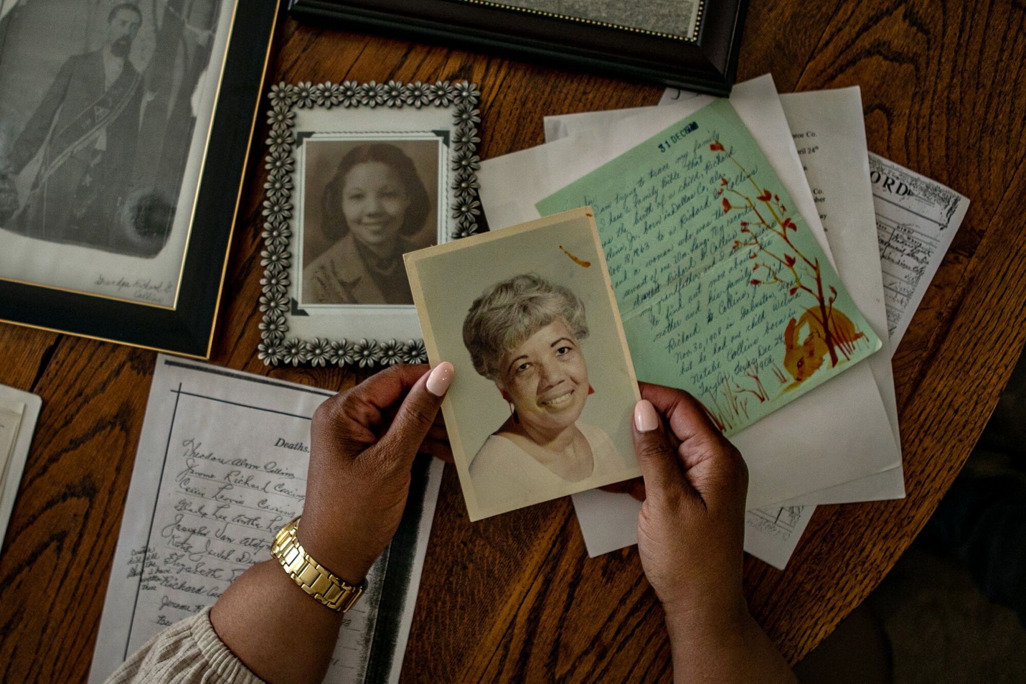A person holds a photo of a woman at a table full of old family documents and pictures.