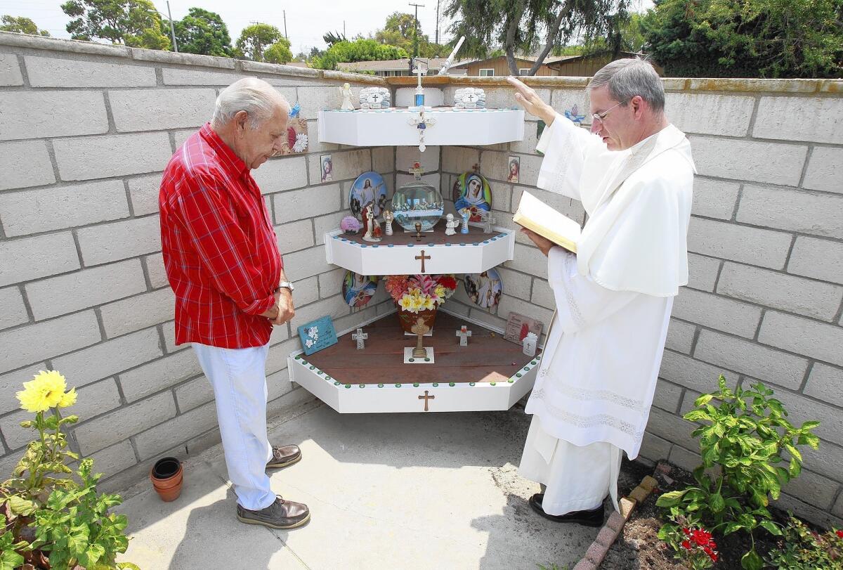 Frank DeSimone, left, listens and prays as Father Augustine Puchner of St. John the Baptist Catholic Church blesses his backyard alter at his home in Costa Mesa last week.