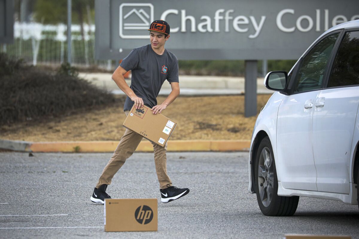 Following social distancing measures, a student picks up a laptop placed in a parking lot.