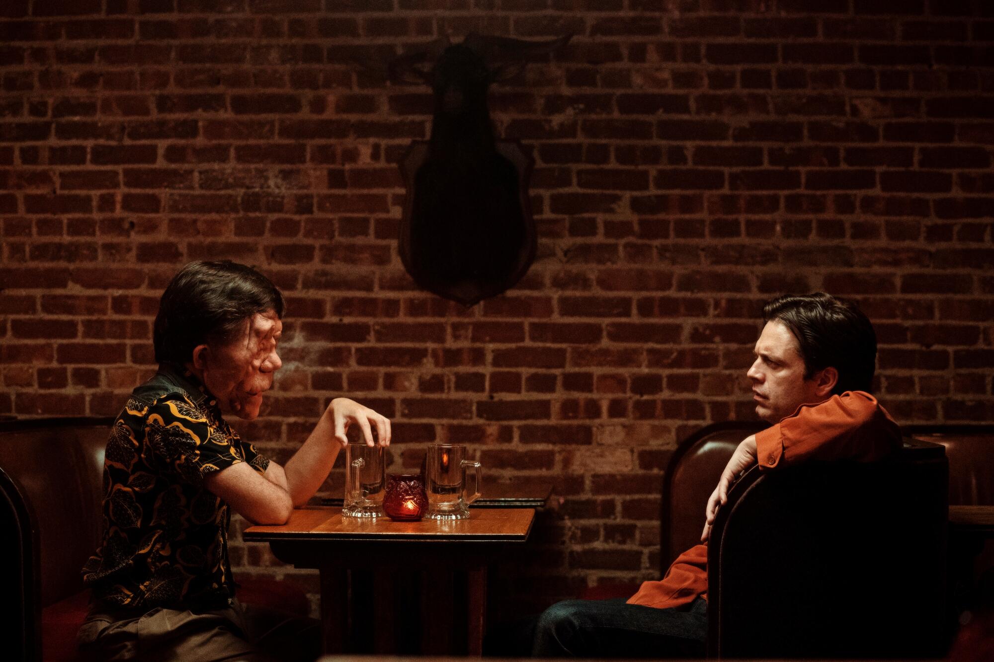 Two men look at each other across a table at a bar.