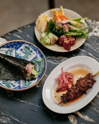 VENICE, CA - MAY 15: (Clockwise from left) A hand roll, a plate of house-pickled and fermented vegetables, and grilled skewers at RVR on May 15, 2025 in Venice, CA. (Shelby Moore / For The Times)