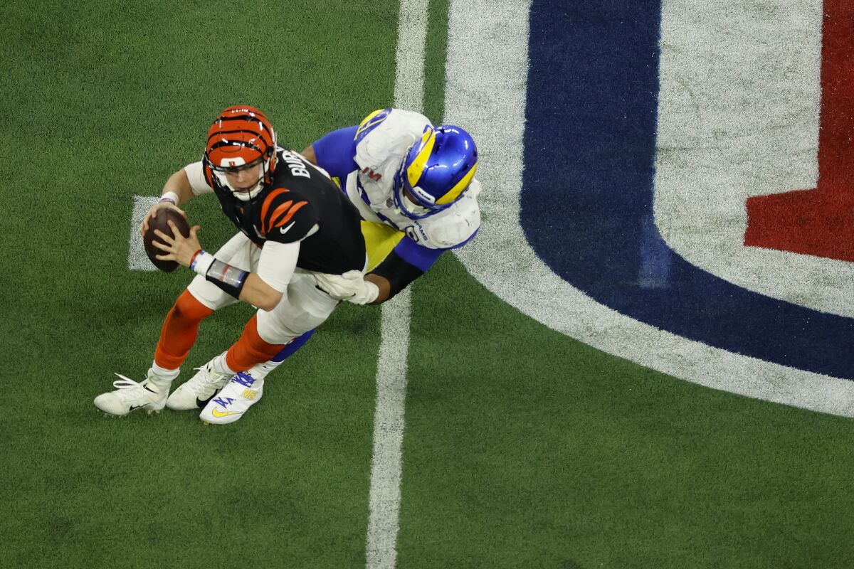 A Bengals player preparing to throw a football is grabbed from behind by a Rams player.