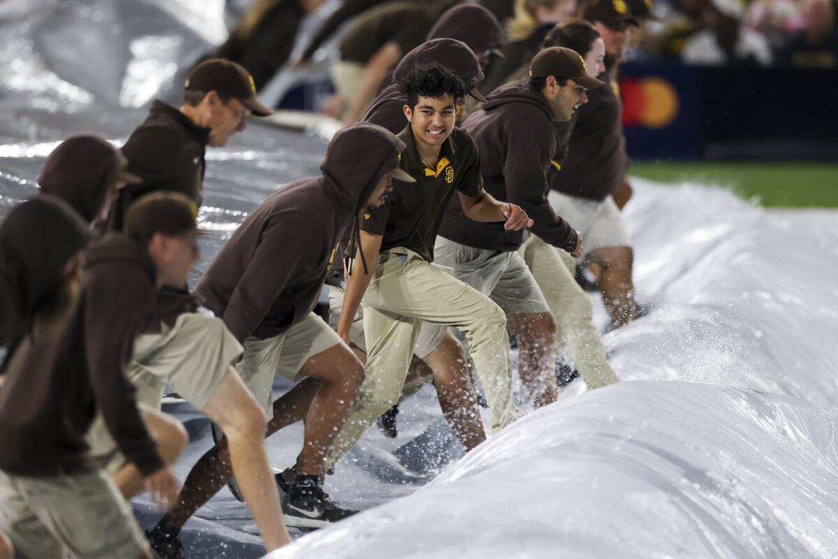 The Padres field crew deploys a tarp on the field at Petco Park before Game 4 of the NLDS on Saturday night