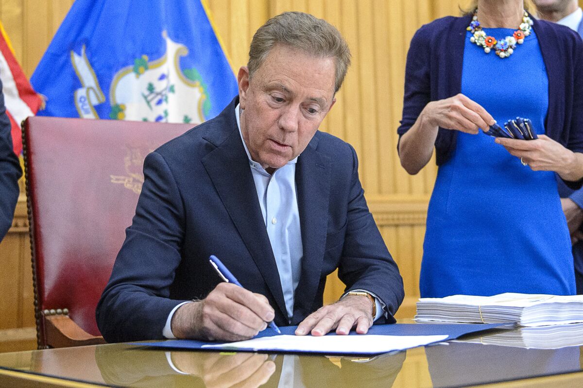 FILE - Connecticut Gov. Ned Lamont signs into law the legalization of recreational-use marijuana on June 22, 2021 in Hartford, Conn. Most eligible Connecticut residents with certain cannabis possession convictions — roughly 44,000 cases — should have their records automatically erased within 60 days, or about a month longer than expected under a state law taking effect Jan. 1, Lamont said Wednesday, Dec. 7, 2022. (Mark Mirko/Hartford Courant via AP)