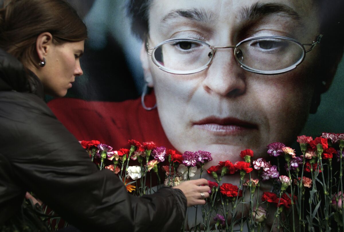 A woman places flowers in front of a large portrait of another woman.