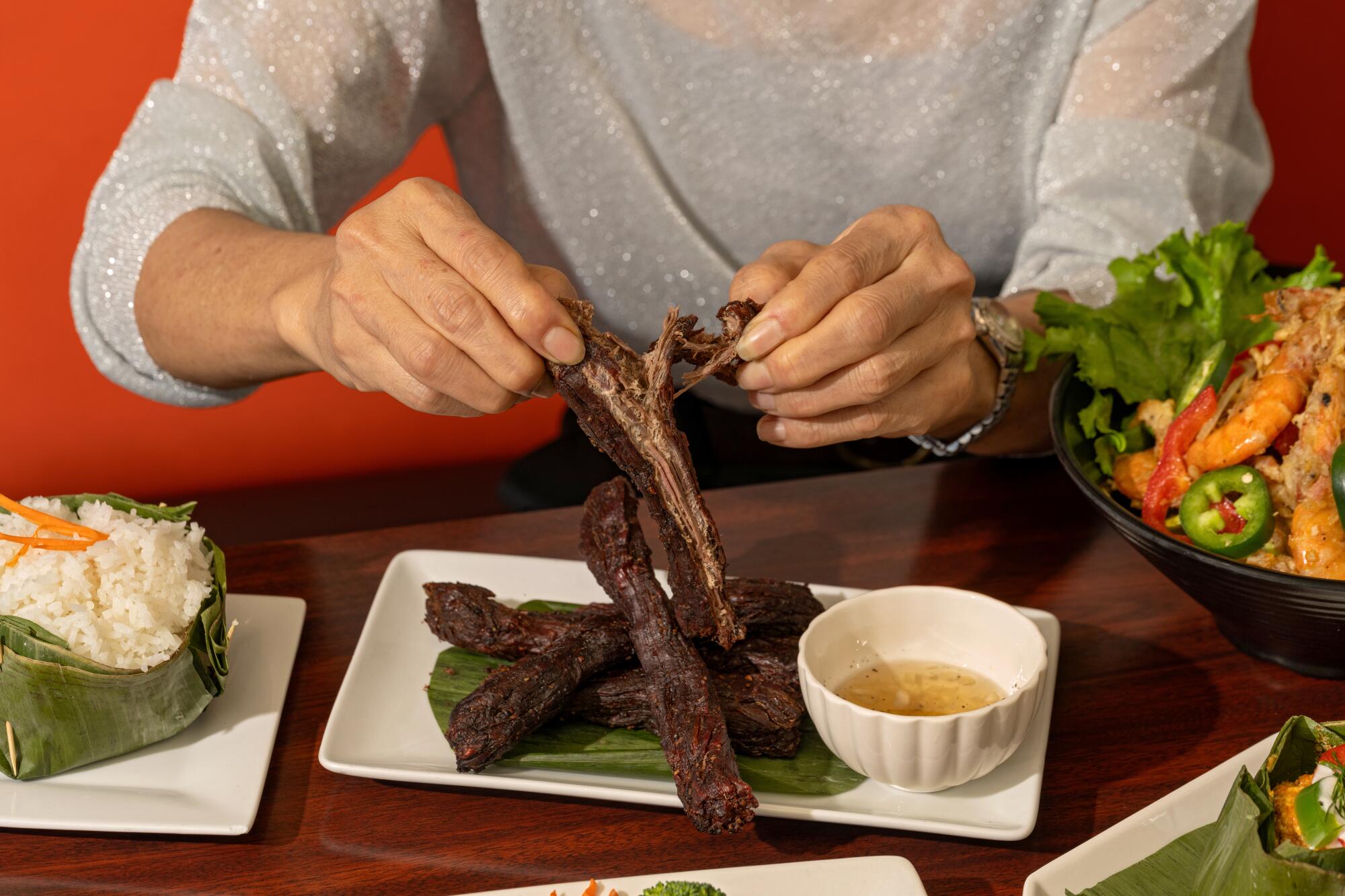 Hands tear into strips of beef jerky at Sophy's: Cambodia Town Food & Music