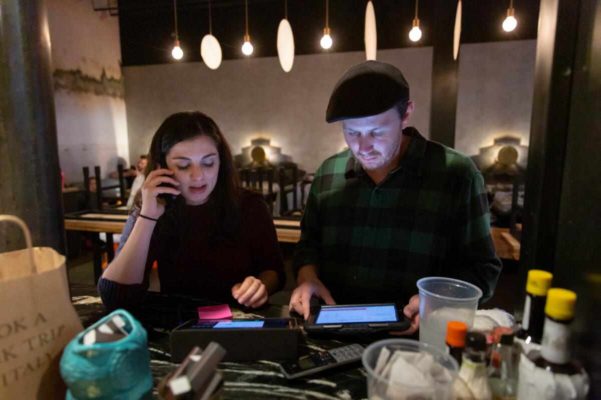 From left, Jessica Morris and Brian O'Farrell call reservations to let them know they can no longer eat in the dining room.