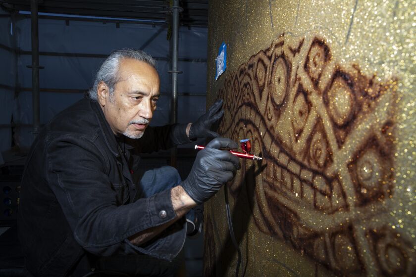 San Diego, California - January 25: Roberto R. Pozos, 60, helps paint a five-story mural called "Brown Image" on a pillar in Chicano Park that features images from car clubs from the 70s on Tuesday, Jan. 25, 2022 in San Diego, California. Eight artists are airbrushing the piece and using techniques that would typically be used to paint a lowrider car. The pillar is being painted a candy apple root beer color mixed with 30 pounds of metal flake which is about 18 cars worth of material. A fundraiser for the volunteer artists will be held on Feb. 5. (Ana Ramirez / The San Diego Union-Tribune)