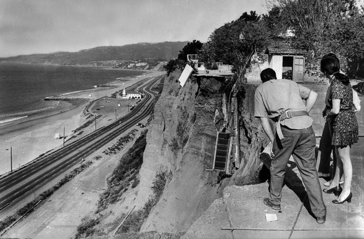 March 3, 1971: Mrs. Carlos Tobaline and her contractor look down on Pacific Coast Highway after 35 feet of the Tobaline family tennis court went down the enbankment. Their Pacific Palisades neighbor's patio, backgound, also went down.