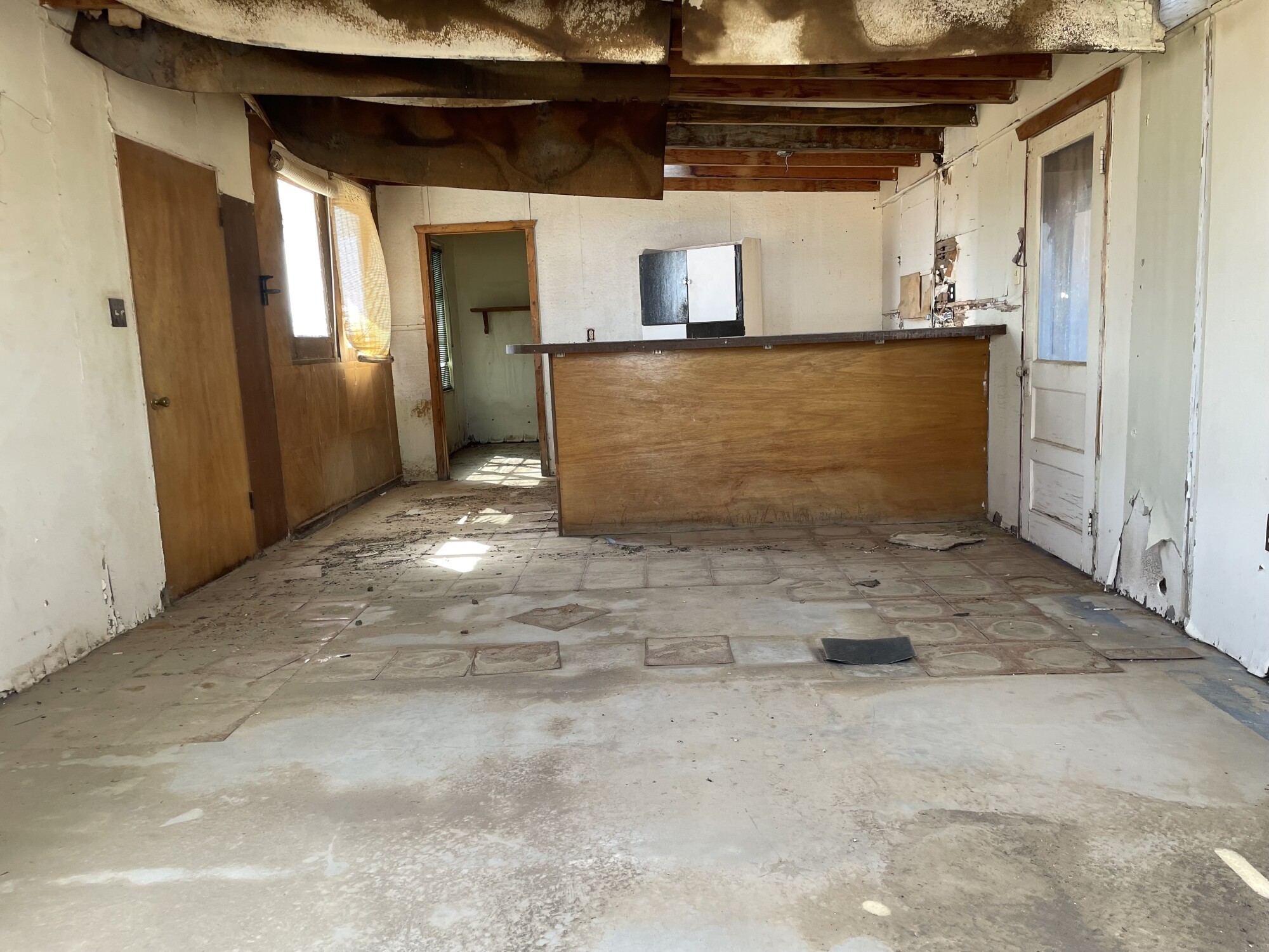 Interior of empty house with partly torn up floor tiles and deteriorating walls and ceiling.