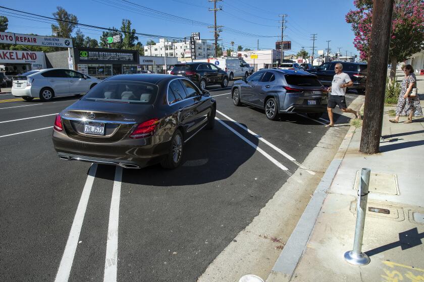 WOODLAND HILLS, CA-AUGUST 28, 2023:Craig Edelson and his wife Sylvie head back to their vehicle parked diagonally as another one attempts to back into a diagonal parking space on the north side of Ventura Blvd. in Woodland Hills. Two weeks ago, the Los Angeles Department of Transportation replaced parallel parking on Ventura Blvd in Woodland Hills with diagonal parking between Ponce And Fallbrook Ave. on both sides of the street. The replacement is part of the "Reimage of Ventura Boulevard" sponsored by city councilmemeber Bob Blumenfield. (Mel Melcon / Los Angeles Times)