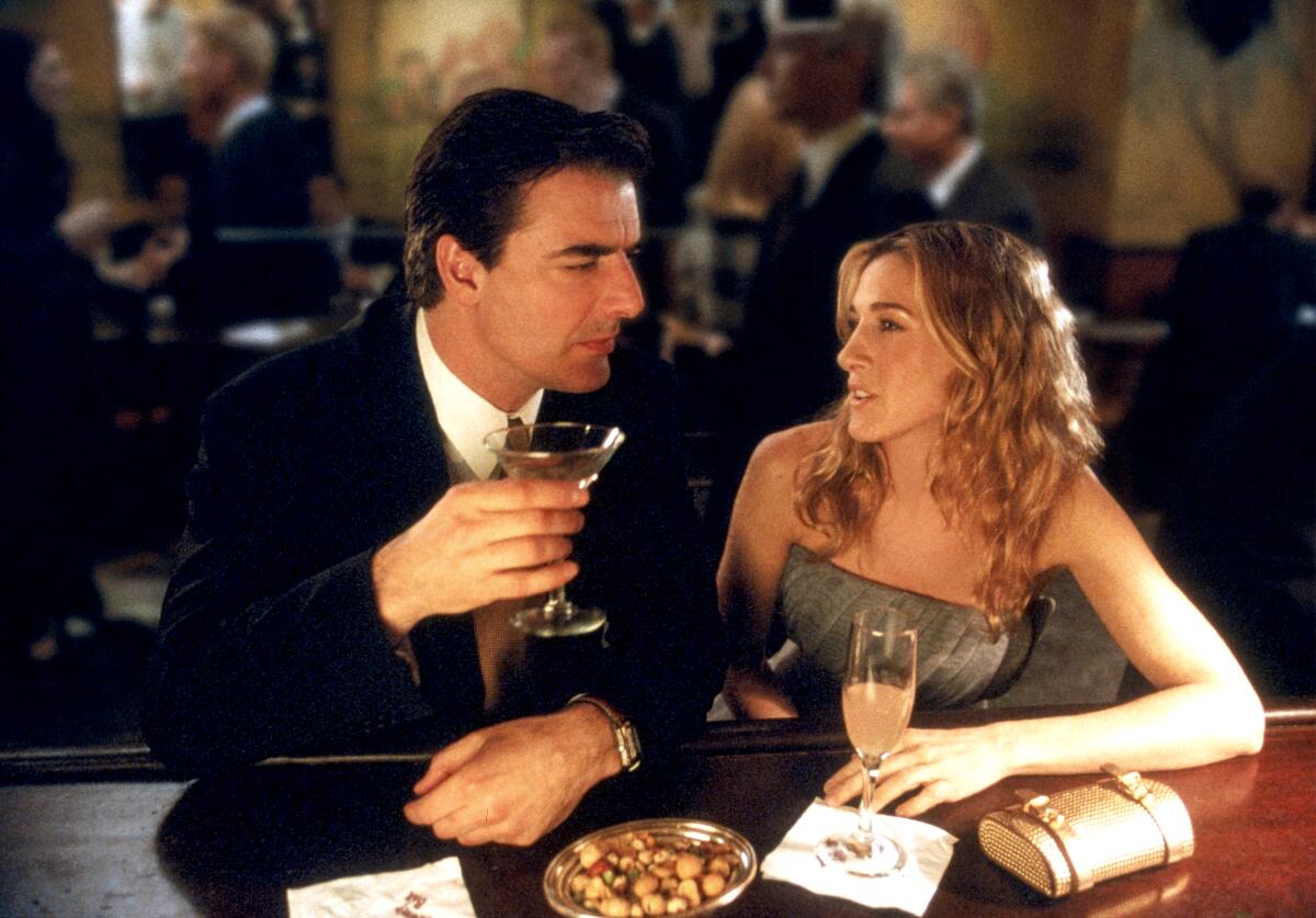 A man holding a martini glass sits next to a woman with a wine glass.