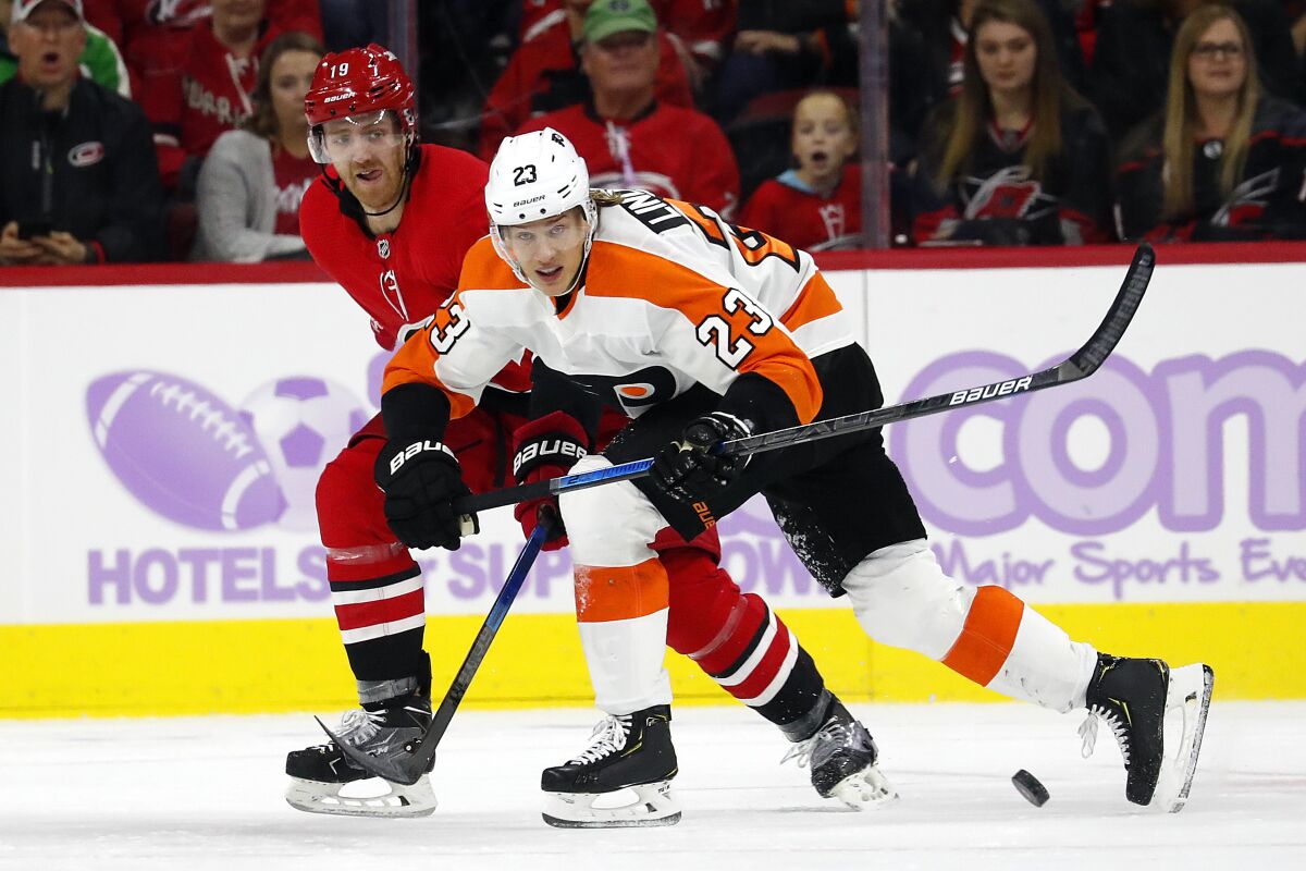 File-Philadelphia Flyers' Oskar Lindblom (23) tries to clear the puck away from Carolina Hurricanes' Dougie Hamilton (19) during the second period of an NHL hockey game in Raleigh, N.C., Thursday, Nov. 21, 2019. Weeks after he completed bone cancer treatments, Lindblom returned to the Philadelphia Flyers to begin the unlikeliest of comebacks. Lindblom says he’s “happier than ever” to be back on the ice and skated with Flyers in Toronto Sunday, Aug. 16, 2020, before they played Montreal in Game 3 of the Eastern Conference playoffs. (AP Photo/Karl B DeBlaker, File)