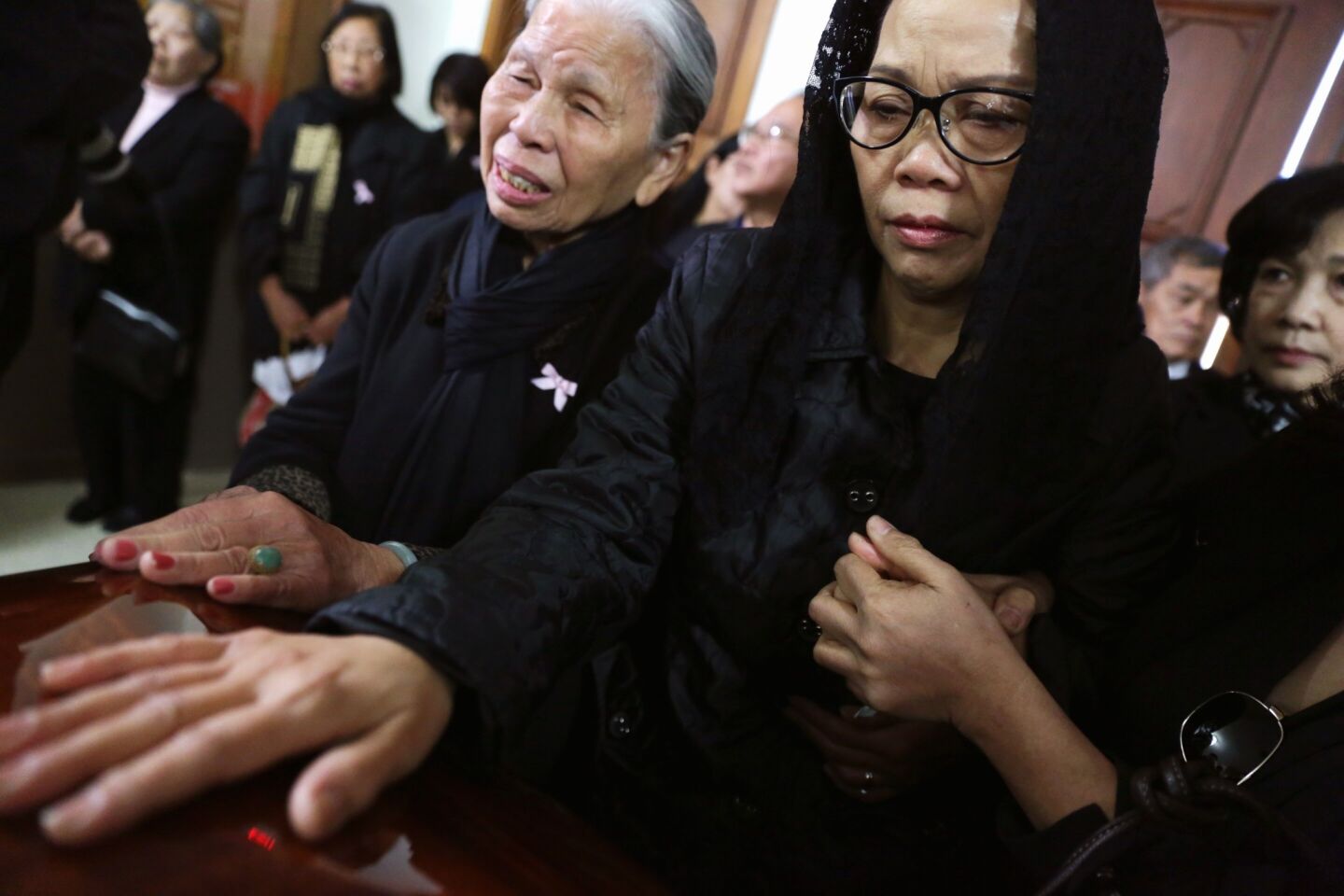 Van Thanh Nguyen places her hand on her daughter's casket while surrounded by friends and family.