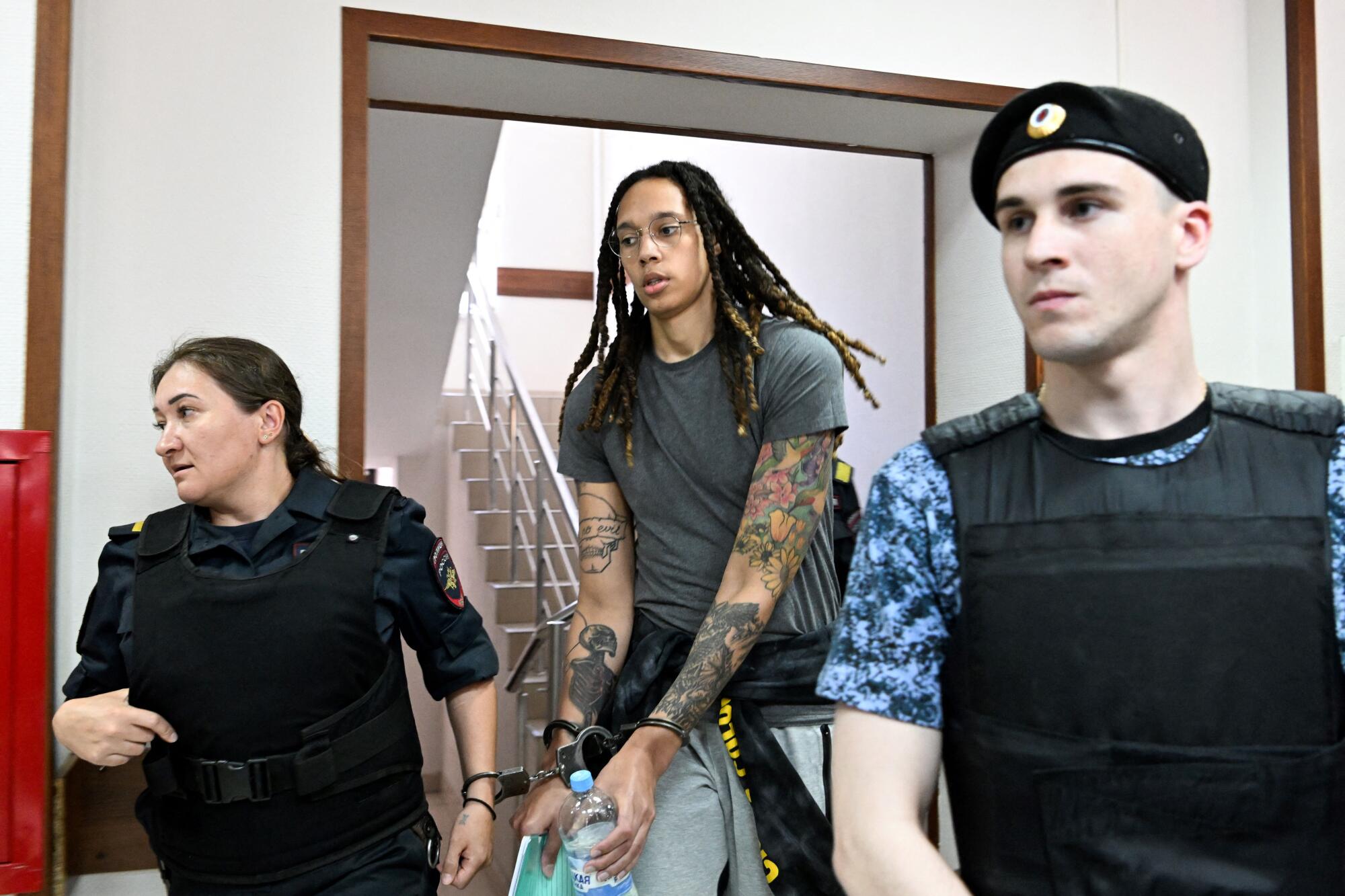 Brittney Griner is escorted by a woman and a man in uniform.